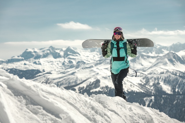 Portrait of happy young woman snowboarder is standing with snowboard in hands. Winter vacations or sports concept