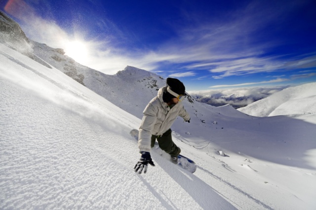Snowboarder doing a toe side carve with deep blue sky in background