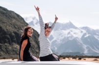 Two happy young girls who are travel lovers enjoy the moment side by side on a roadtrip. They are on top of the van laughing in front of the mountains and getting lost in the nature.Travel concept. Two happy young girls who are travel lovers enjoy the moment side by side on a roadtrip. They are on top of the van laughing in front of the mountains and getting lost in the nature. Working Holiday New Zealand.